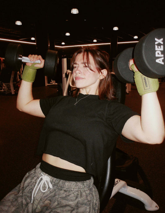 athlete in gym performing shoulder press exercise using uppper wrist wraps in green color
