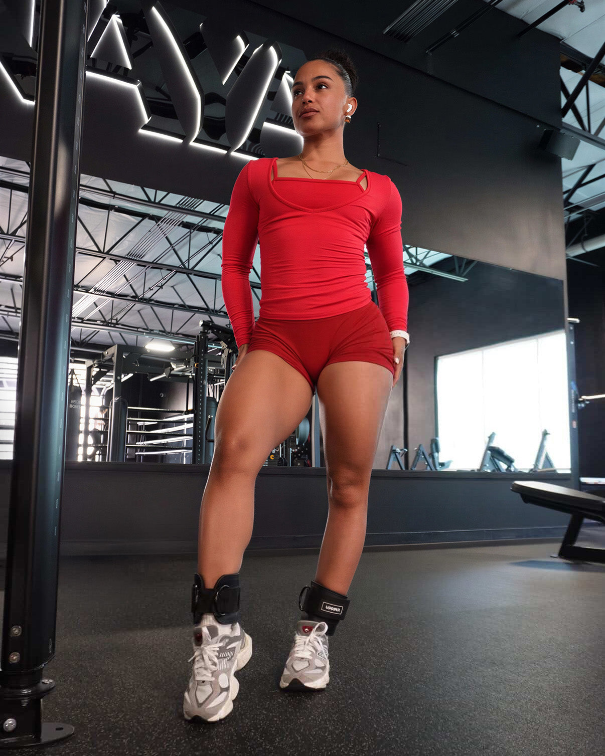 athlete in red gym outfit standing with black uppper ankle straps in dark gym