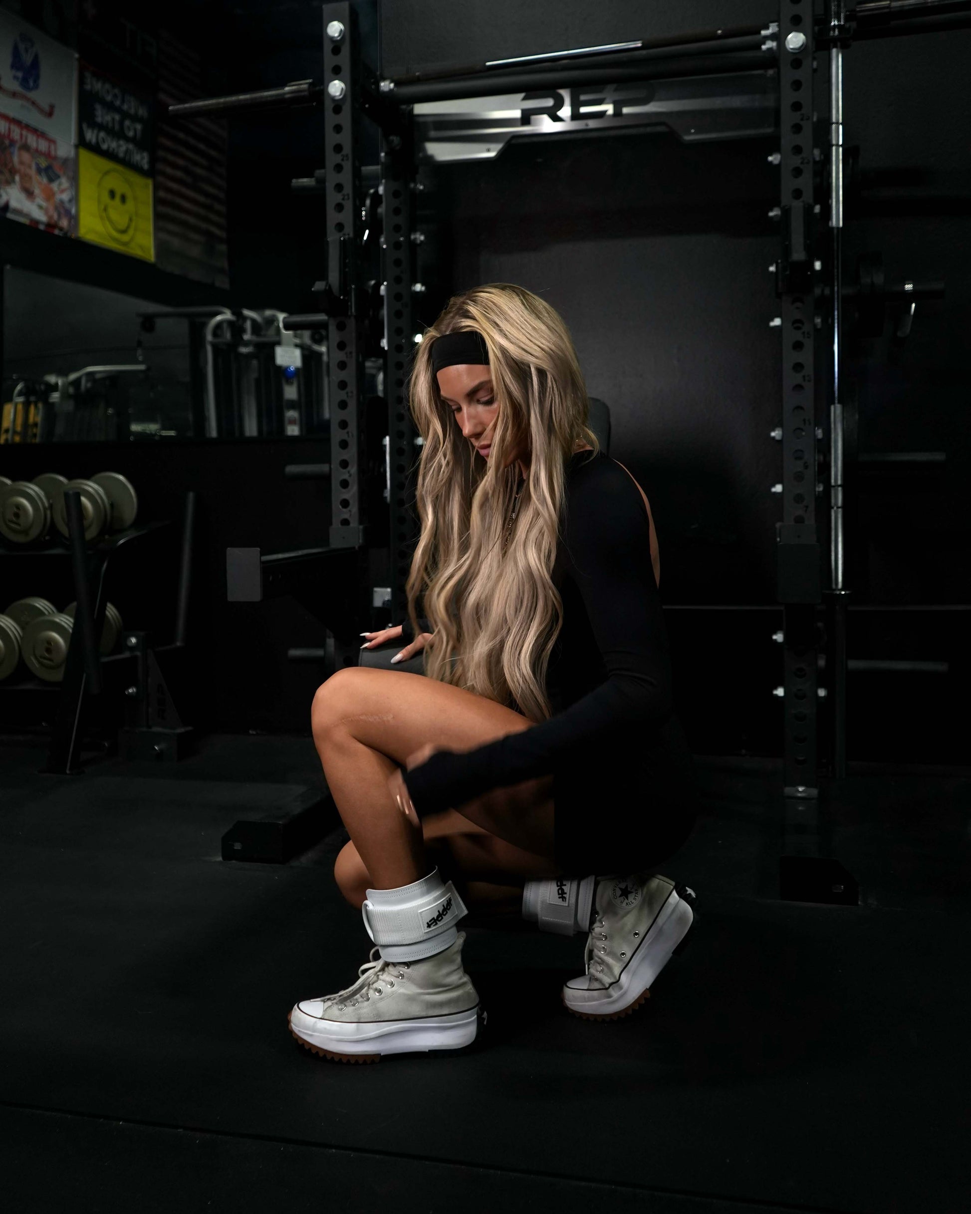 athlete in black gym outfit seated wearing white uppper ankle straps 2.0 in dark gym