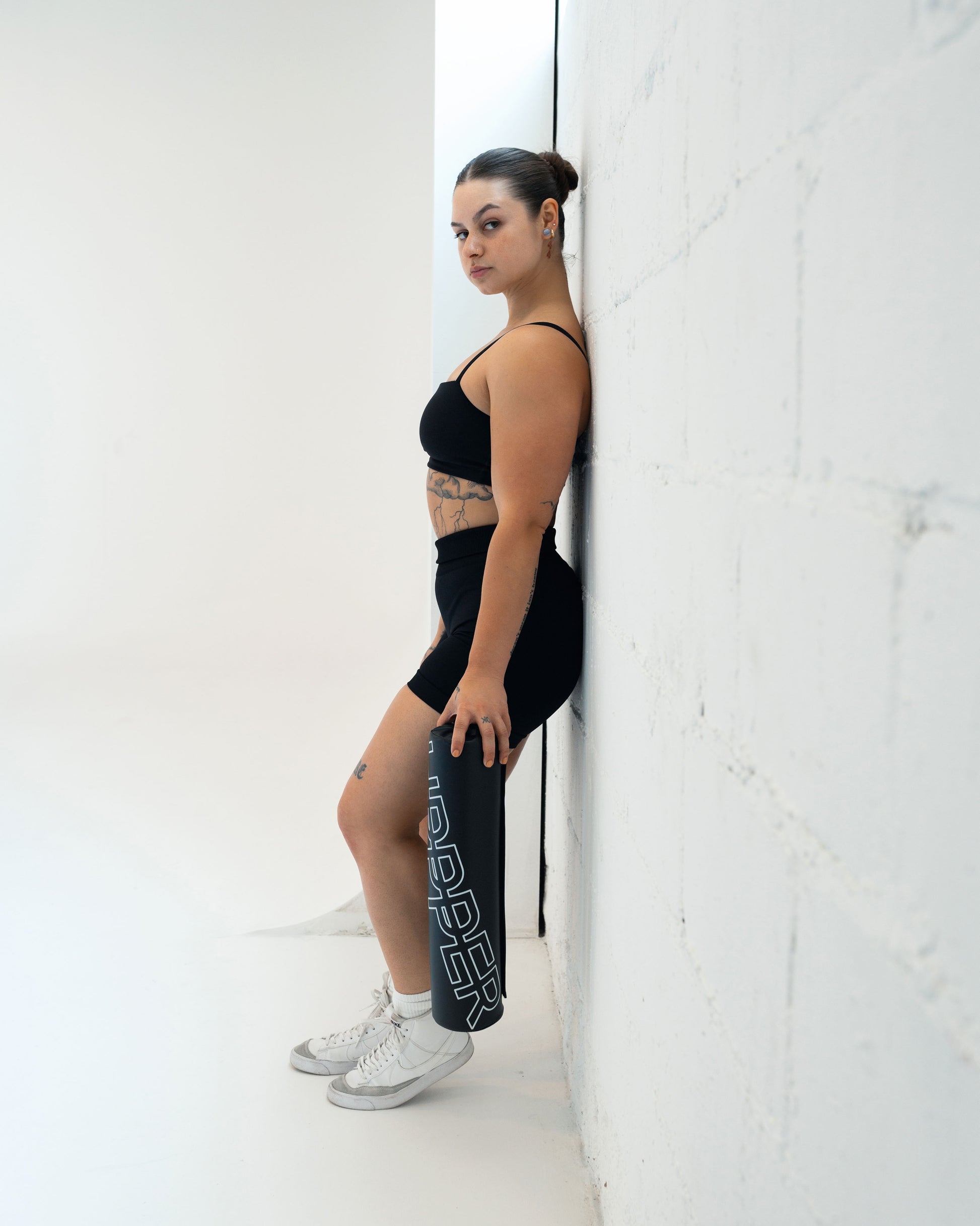 athlete in gym clothes posing with black uppper barbell pad in a light background