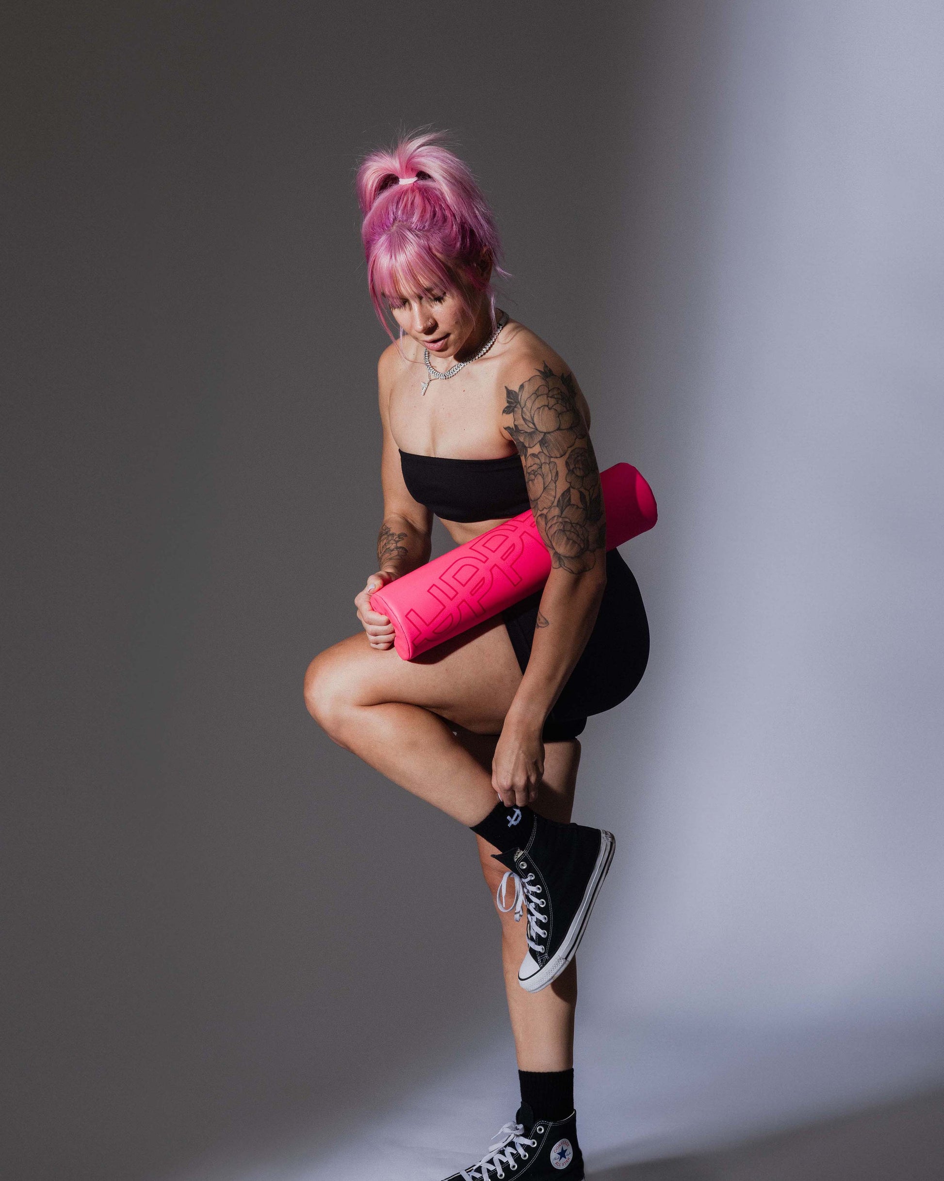 model posing in studio with neon pink uppper barbell pad on grey background