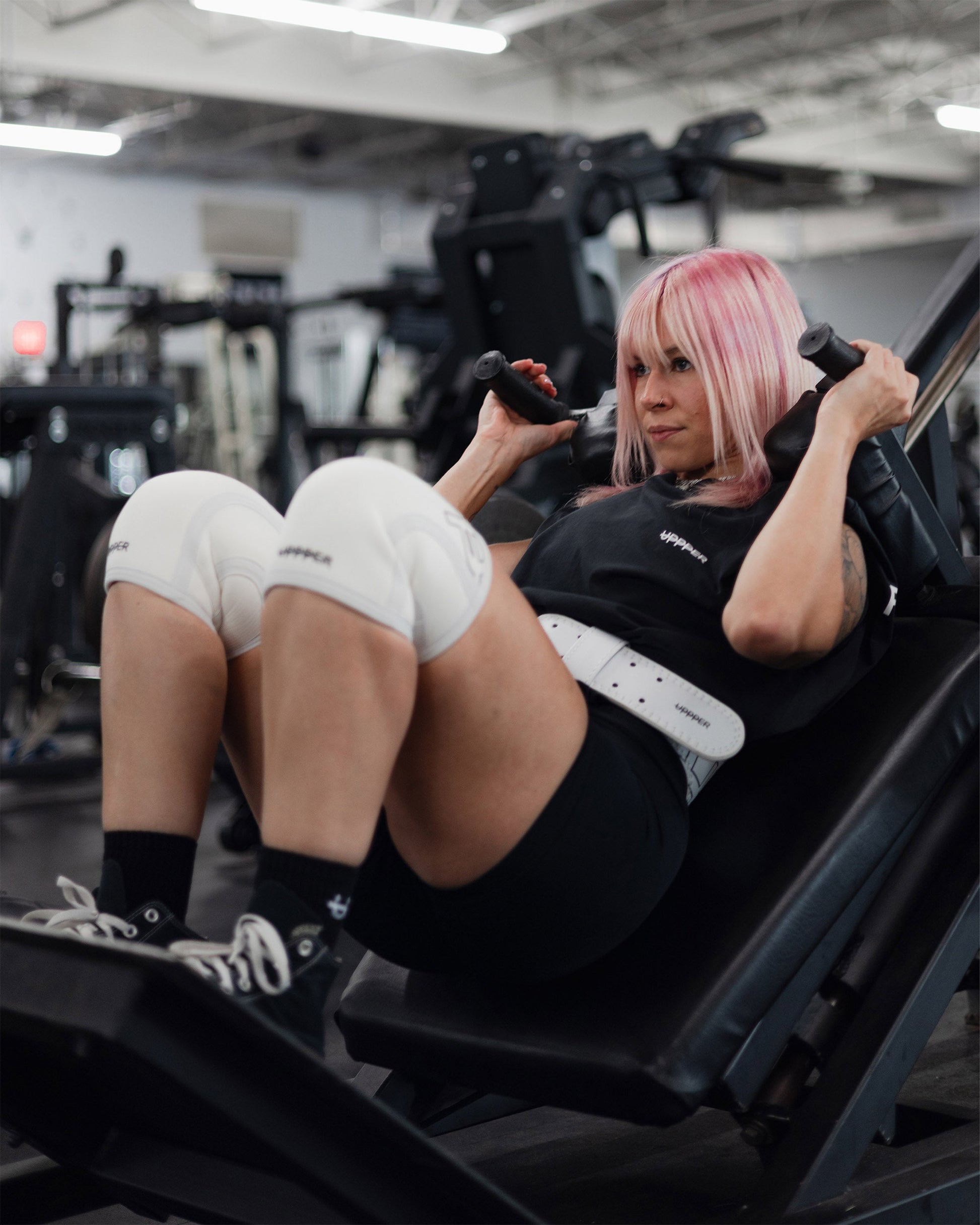 athlete performing exercise wearing white uppper knee sleeves lifting belt and black cre socks with U logo