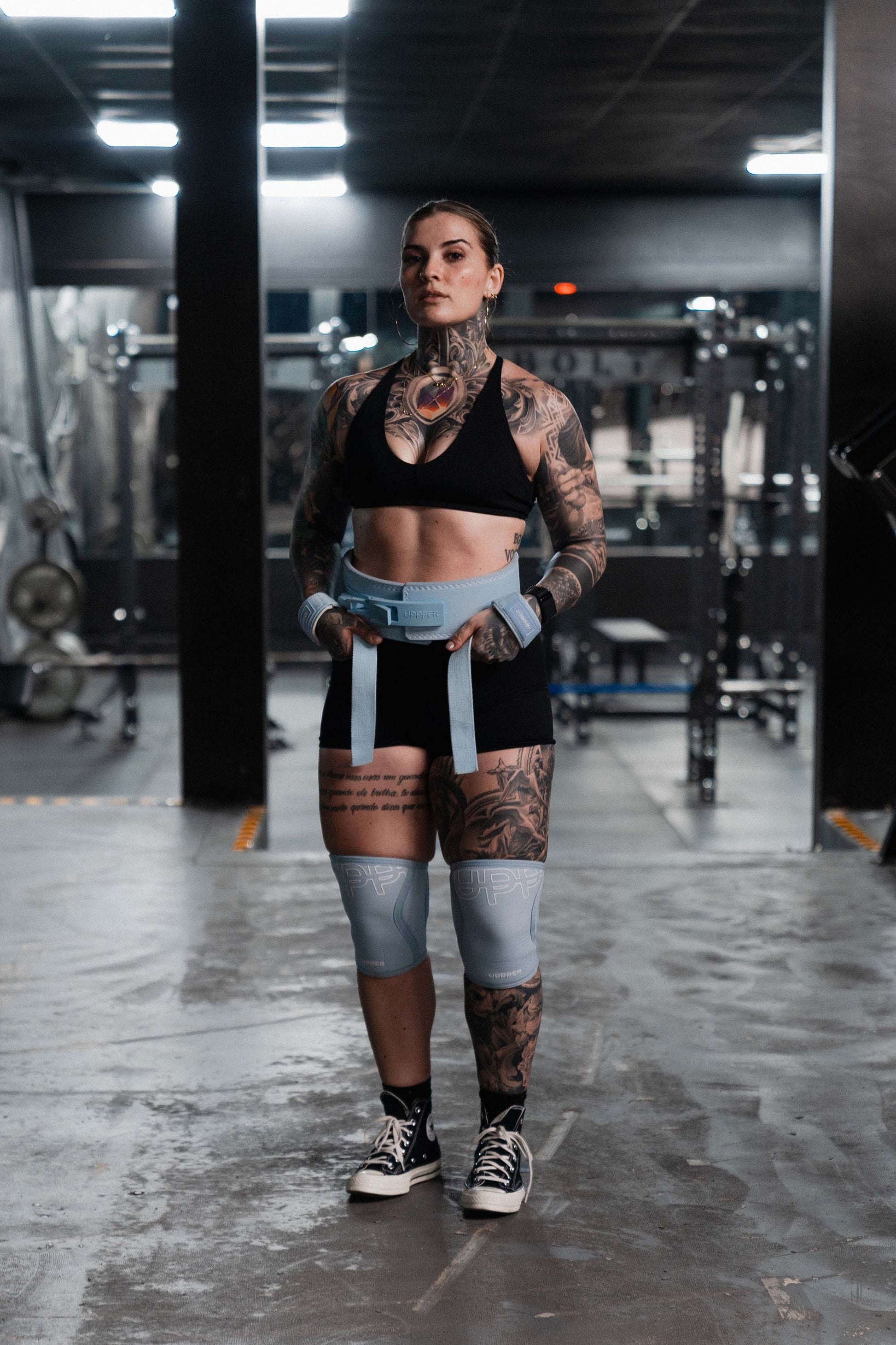 athlete wearing baby blue uppper lever belt, lifting straps and knee sleeves in gym
