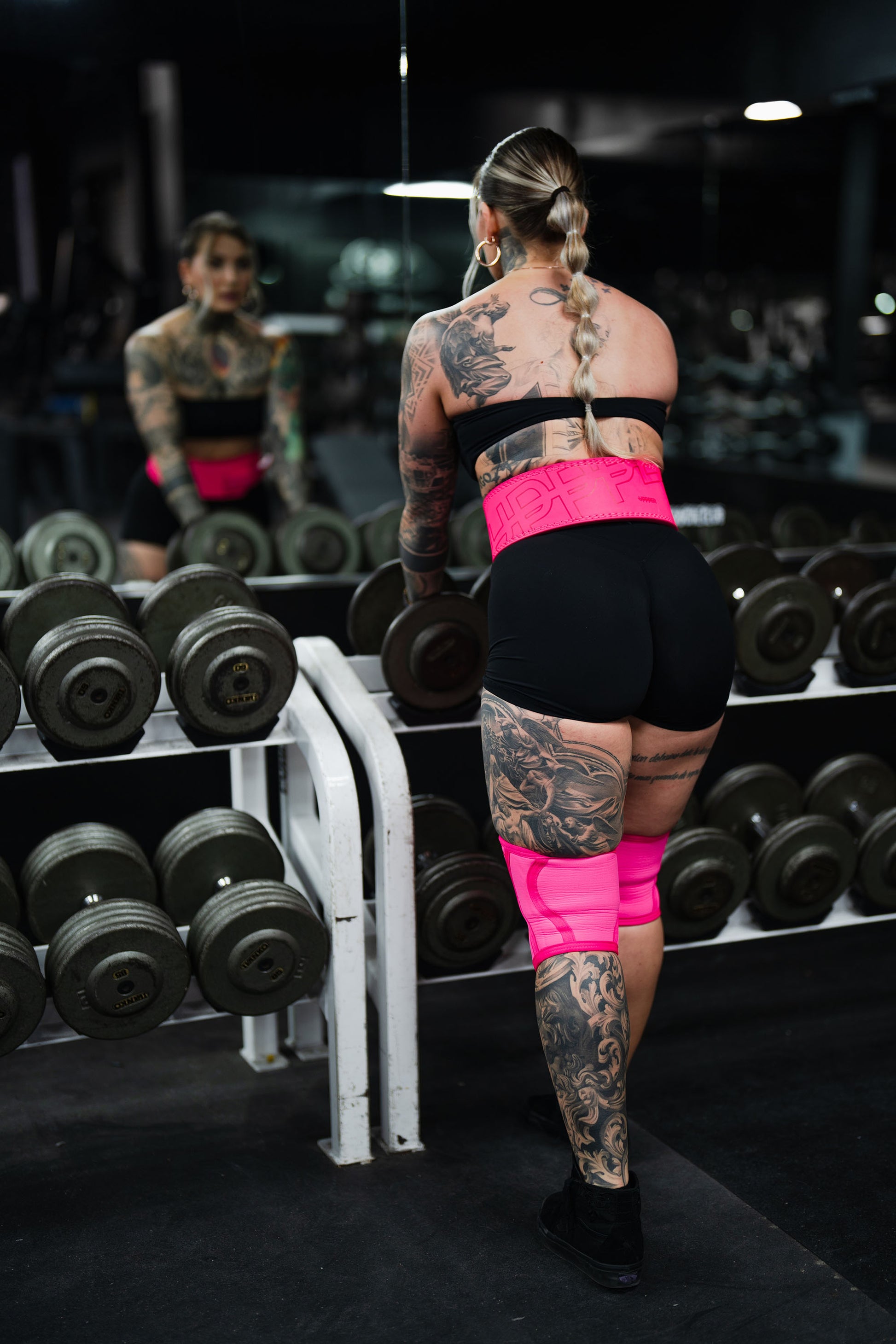woman wering neon pink uppper lever belt and knee sleeves in the gym