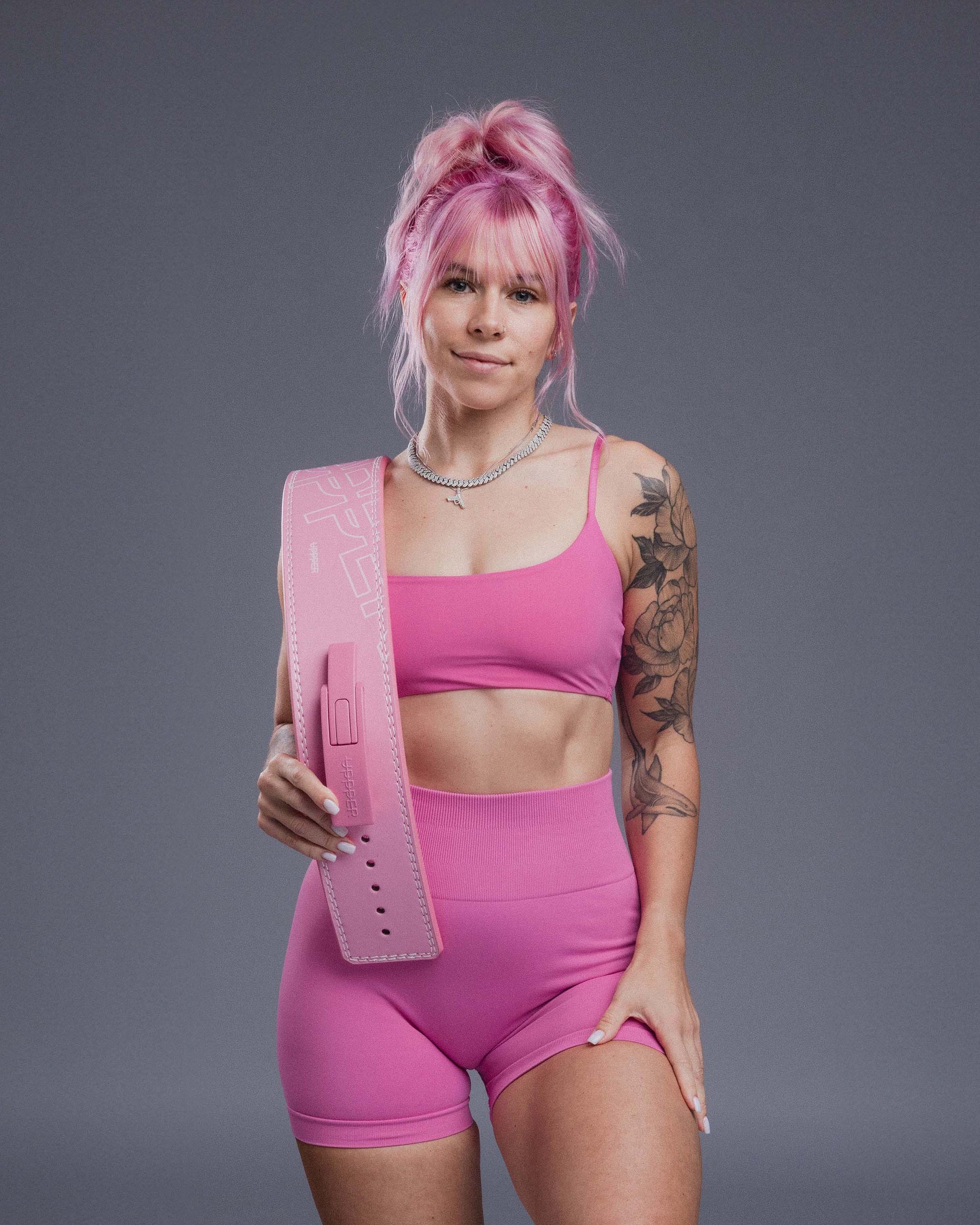 athlete in pink gym outfit holding pink uppper lever belt on grey background