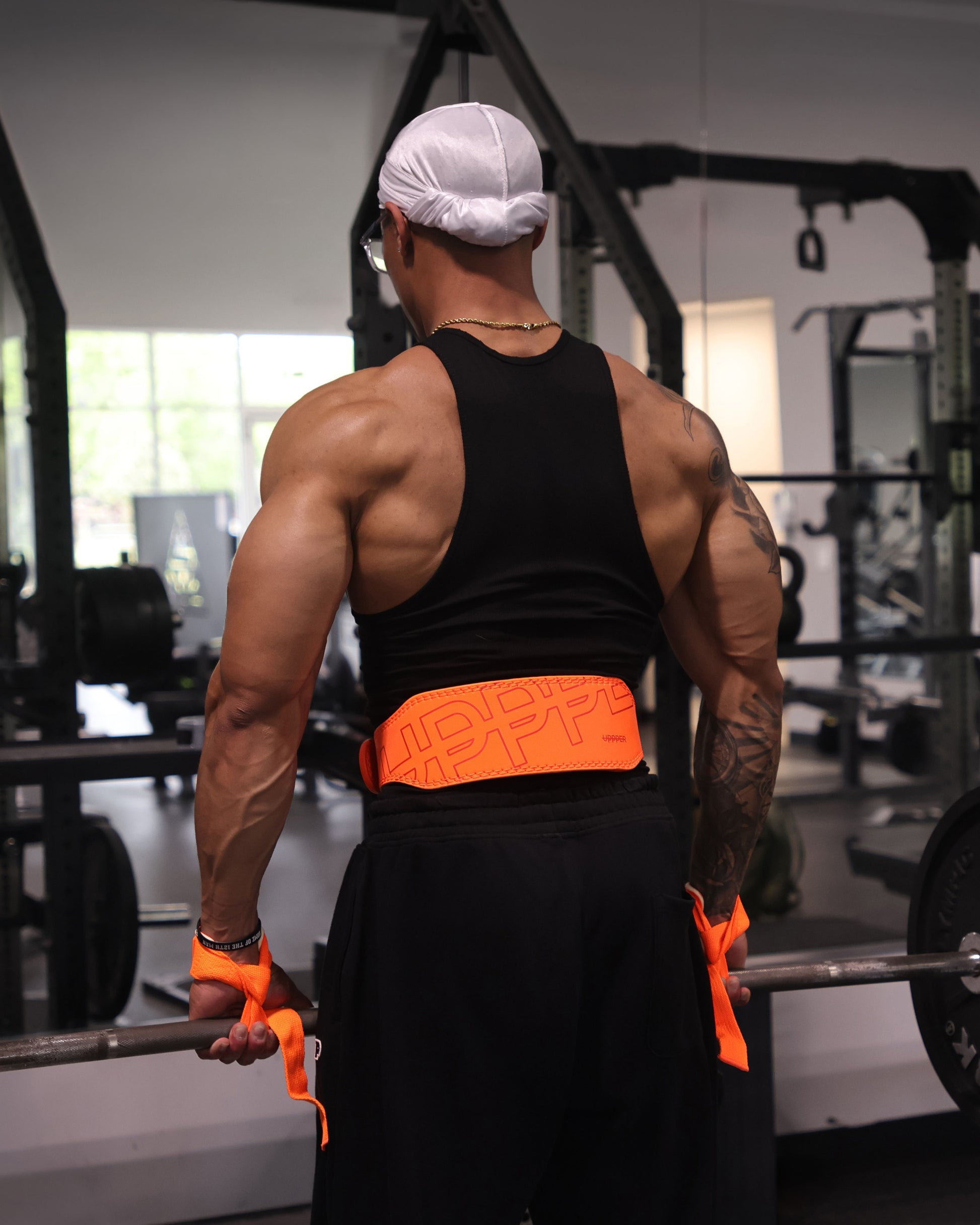 athlete shot from the back performing deadlift exercise wearing uppper lifting belt and straps in neon orange color 
