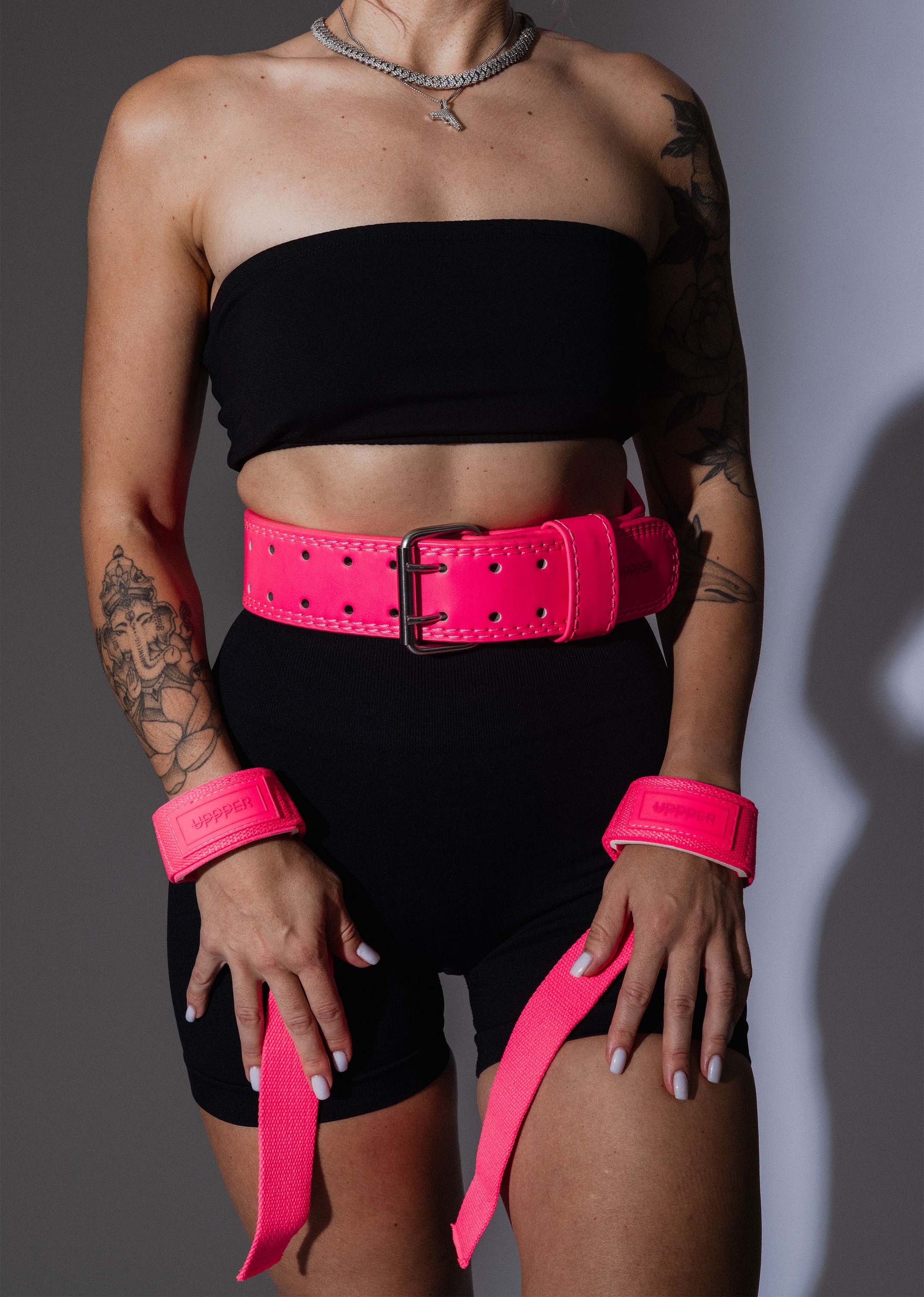 woman wearing neon pink uppper lifting belt and lifting straps on the grey background