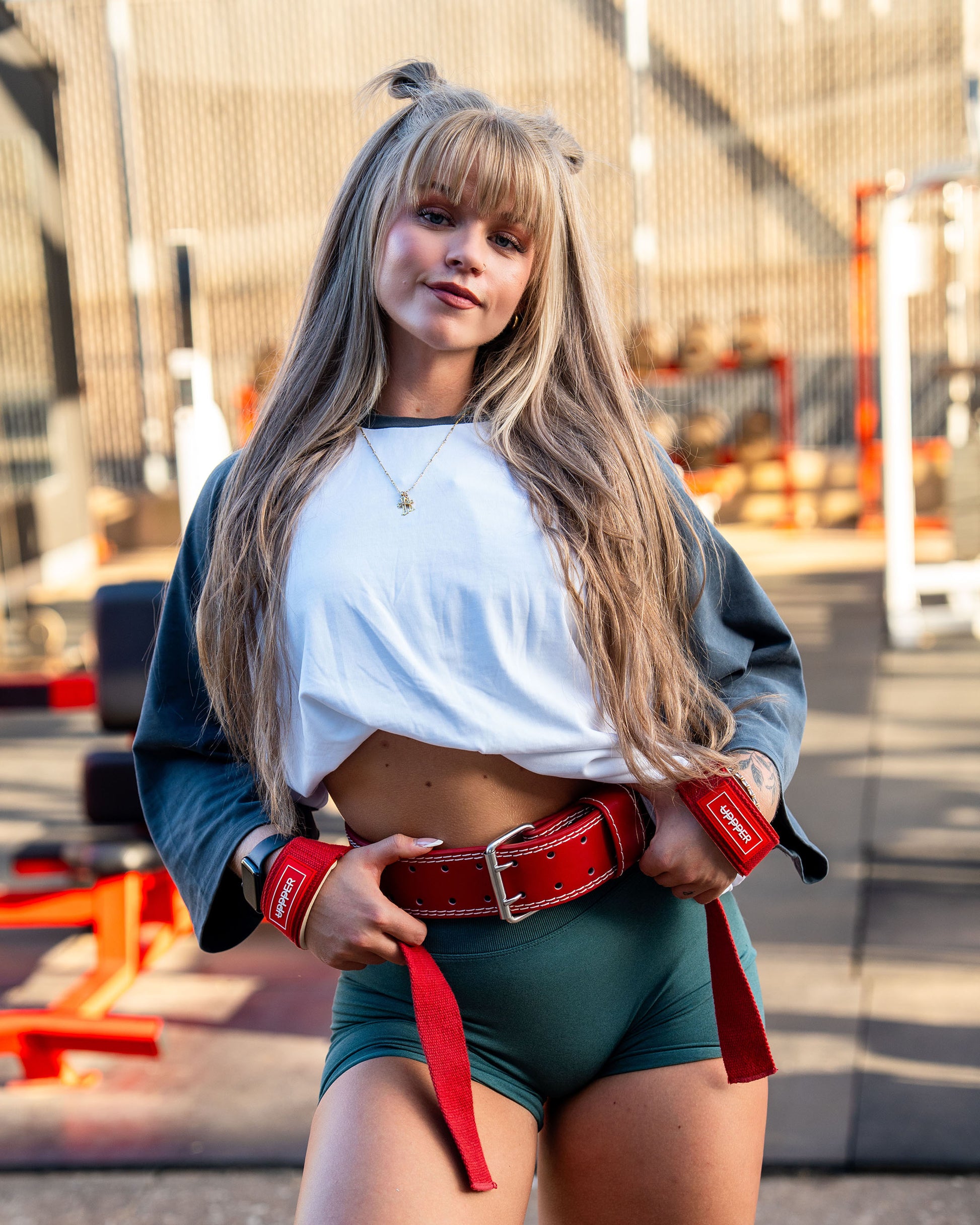 woman wearing a white top green shorts and uppper red lifting belt and straps outdoors