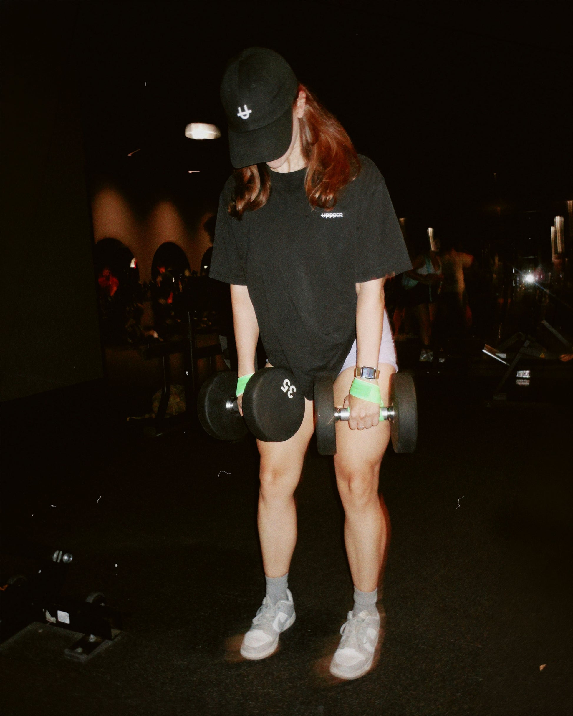 athlete in gym in black hat and black uppper t-shirt performing exercise with dumbbell using uppper lifting straps in neon green color