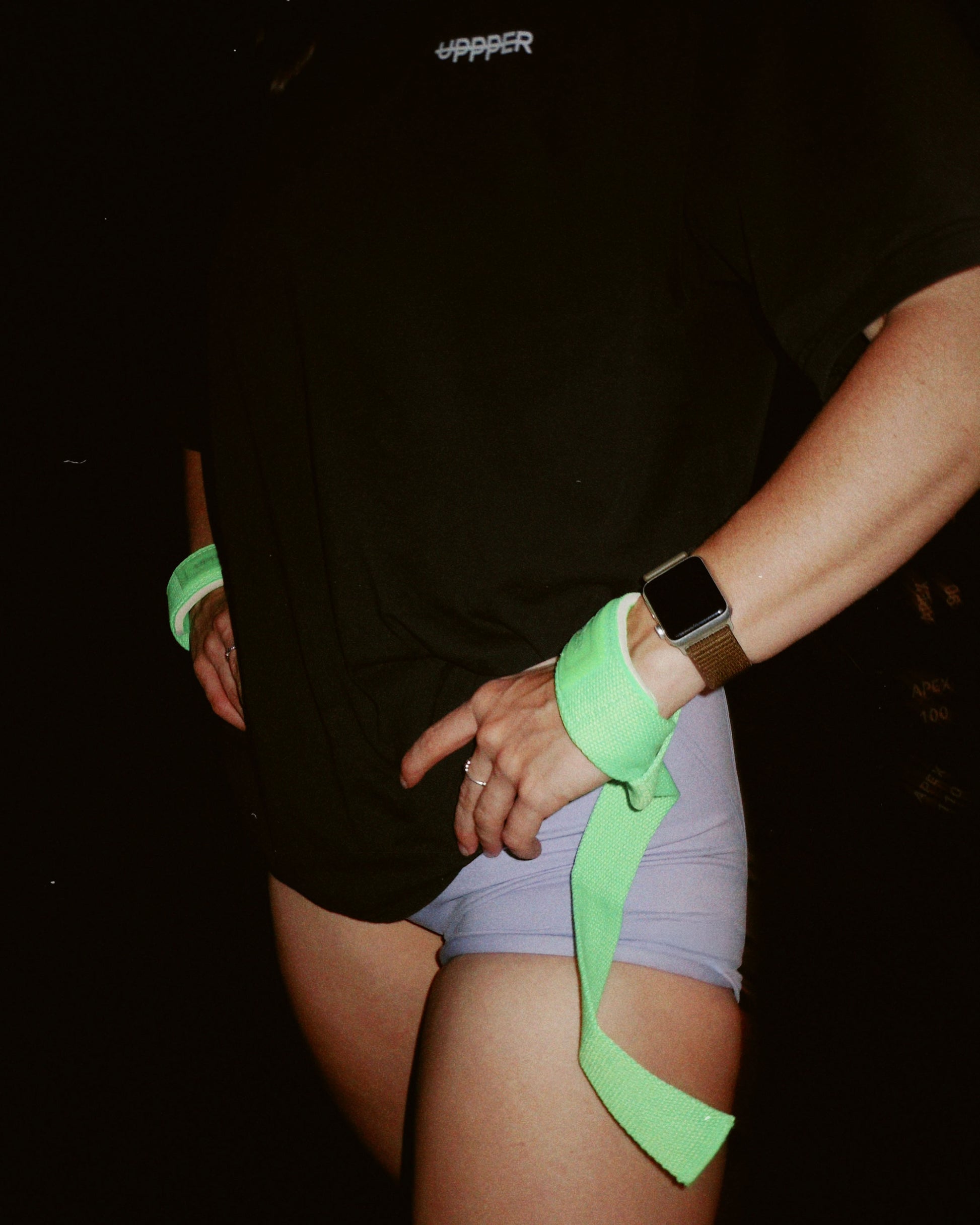 person holding hands with uppper neon green lifting straps against a dark background
