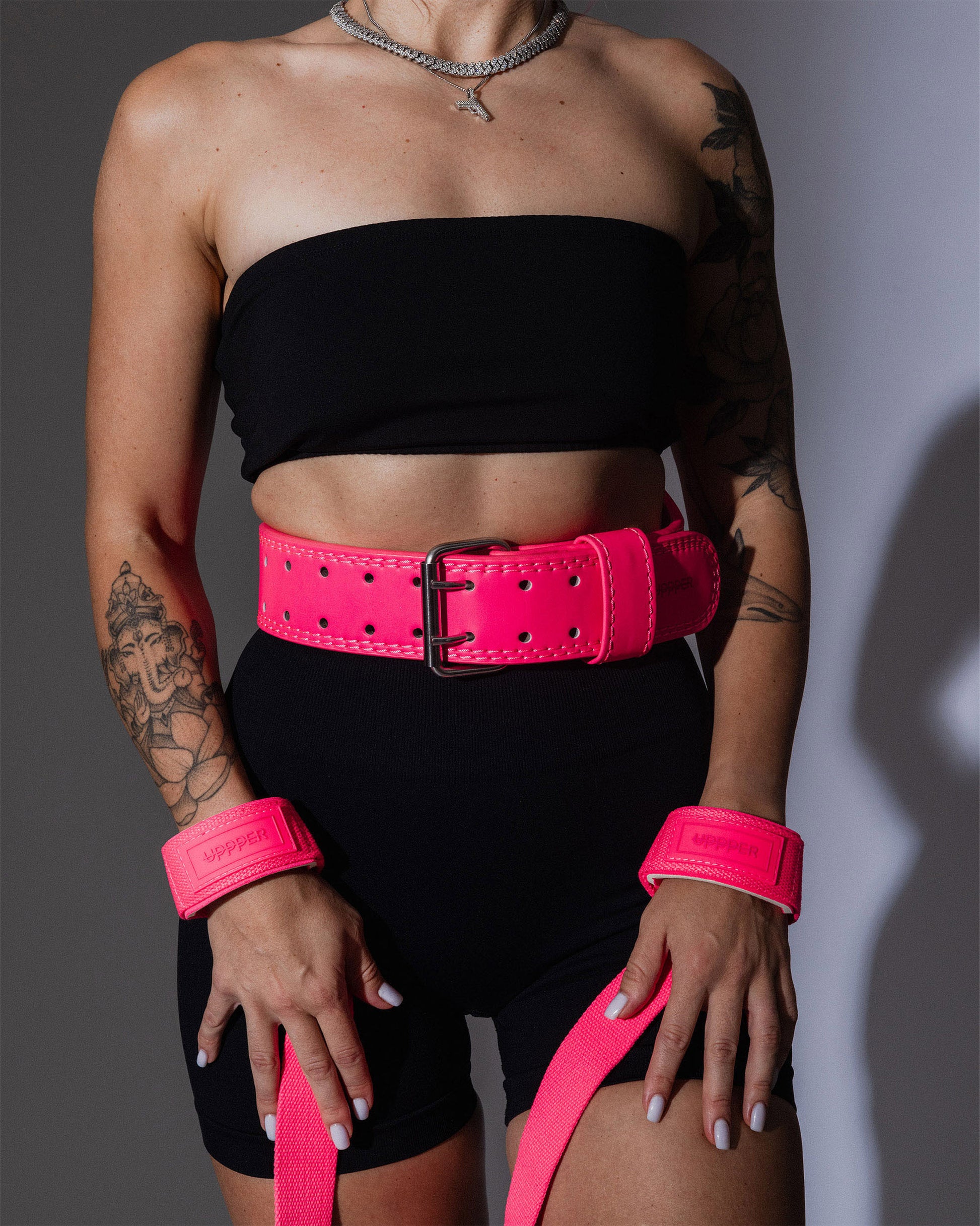 athlete posing in neon pink uppper lifting strap and lifting belt