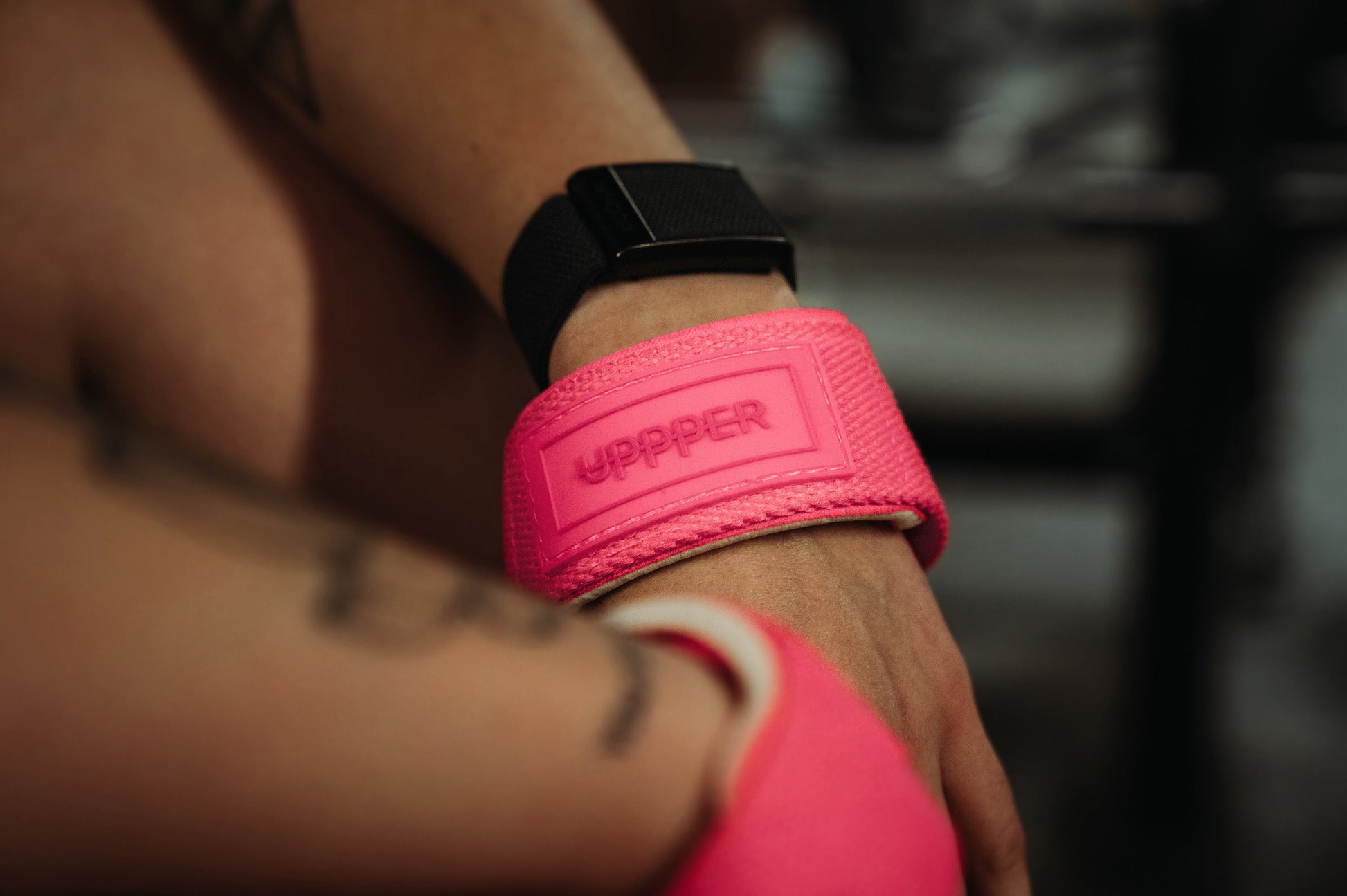 neon pink uppper lifting straps looped around wrist showing logo