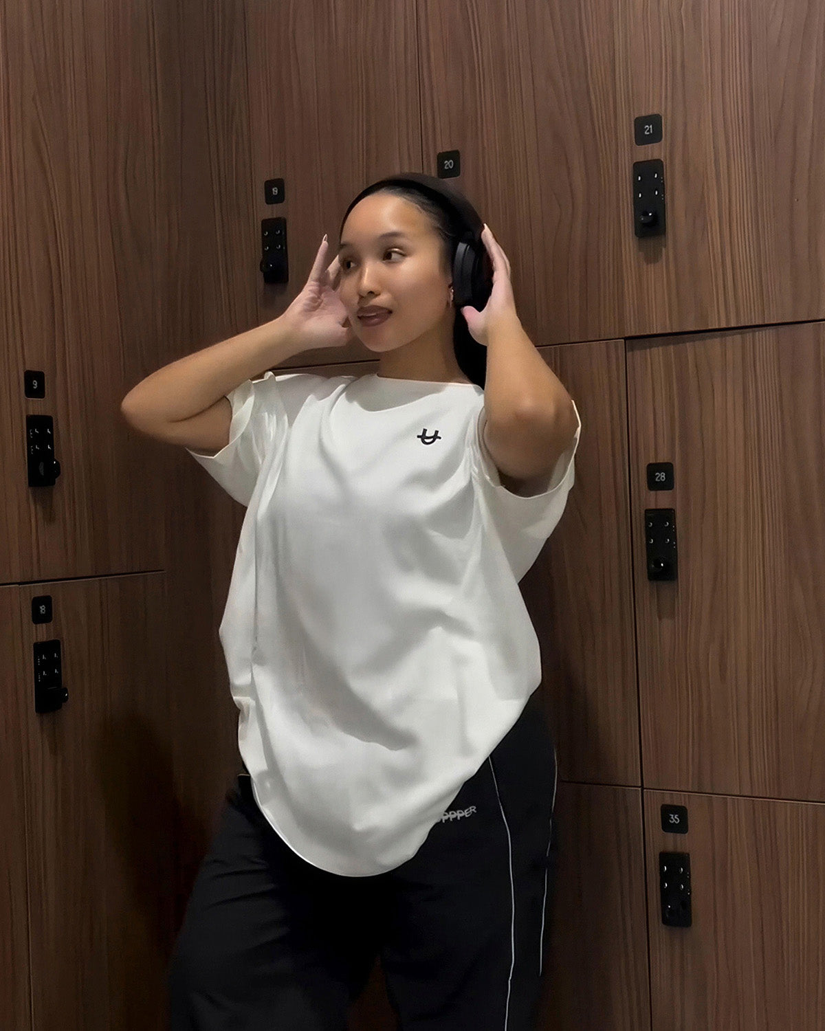 woman wearing white uppper t-shirt adjusting headphones in gym locker room