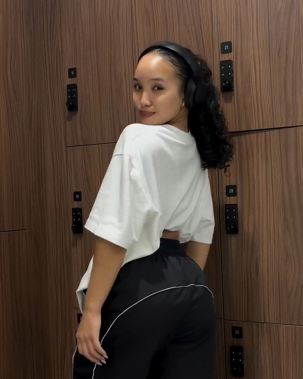woman looking over shoulder showing back of white uppper soft stretch t-shirt in gym locker room