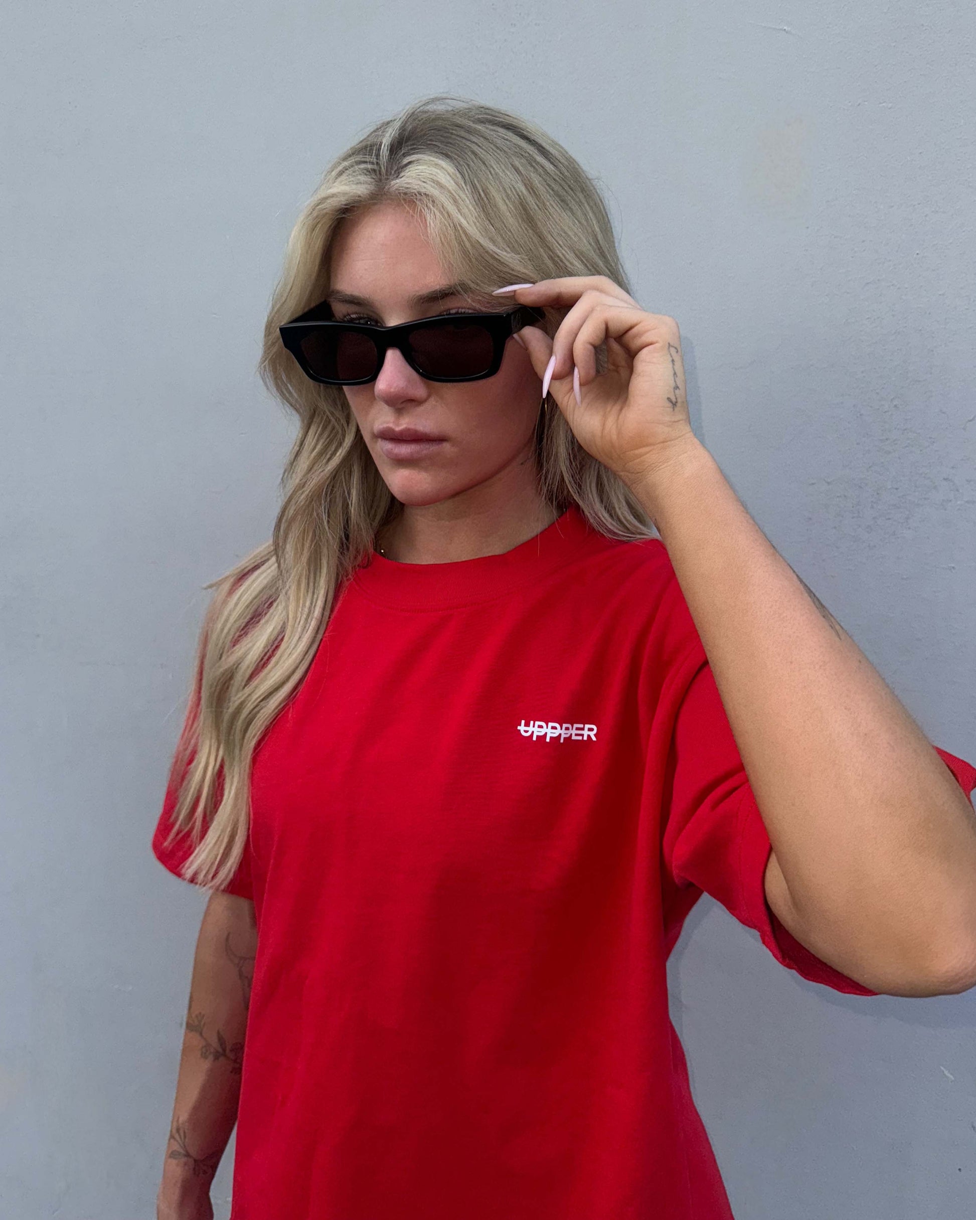 woman wearing red uppper premium fitness gear t-shirt with sunglasses against grey wall