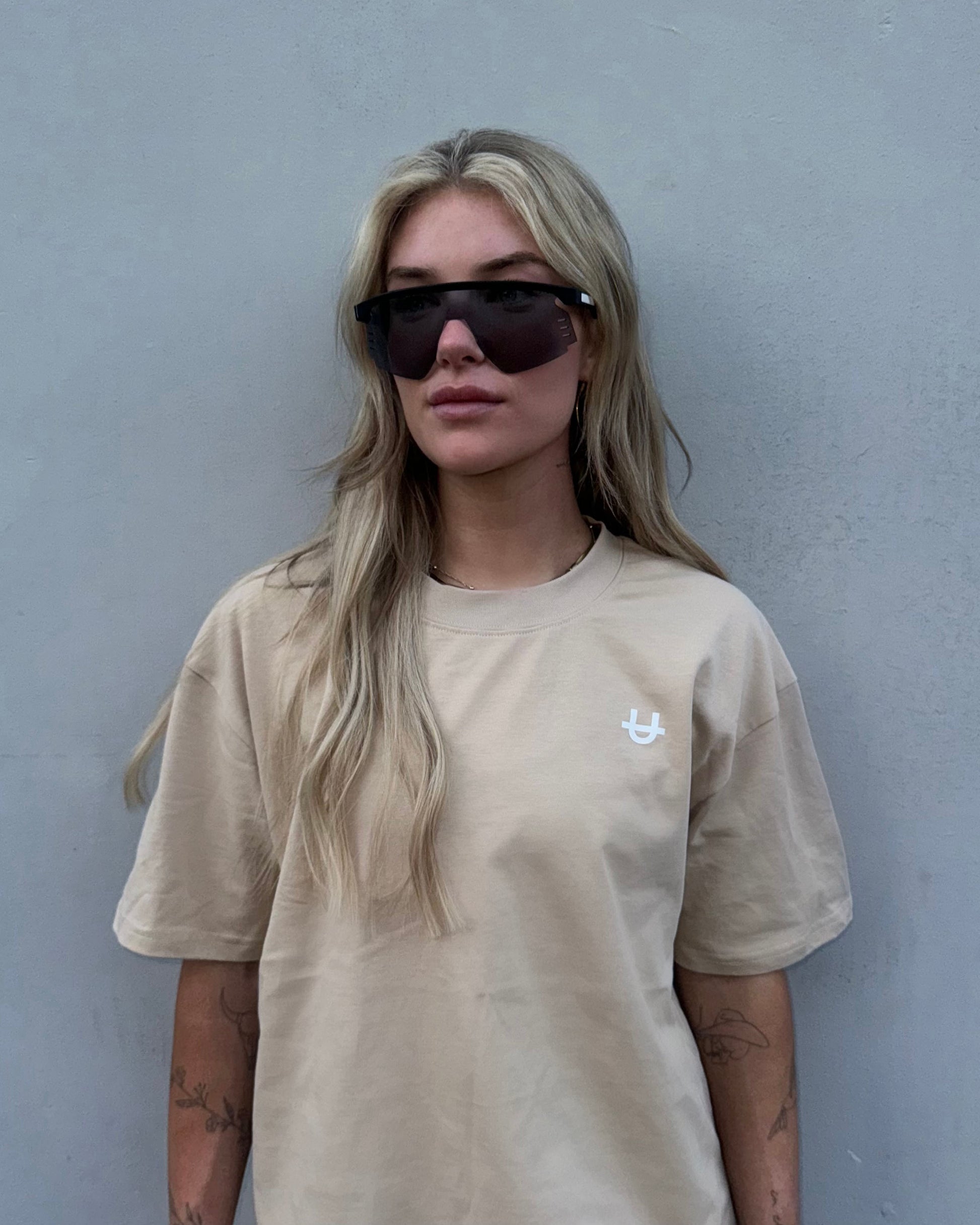woman wearing white uppper core t-shirt with sunglasses against a grey wall